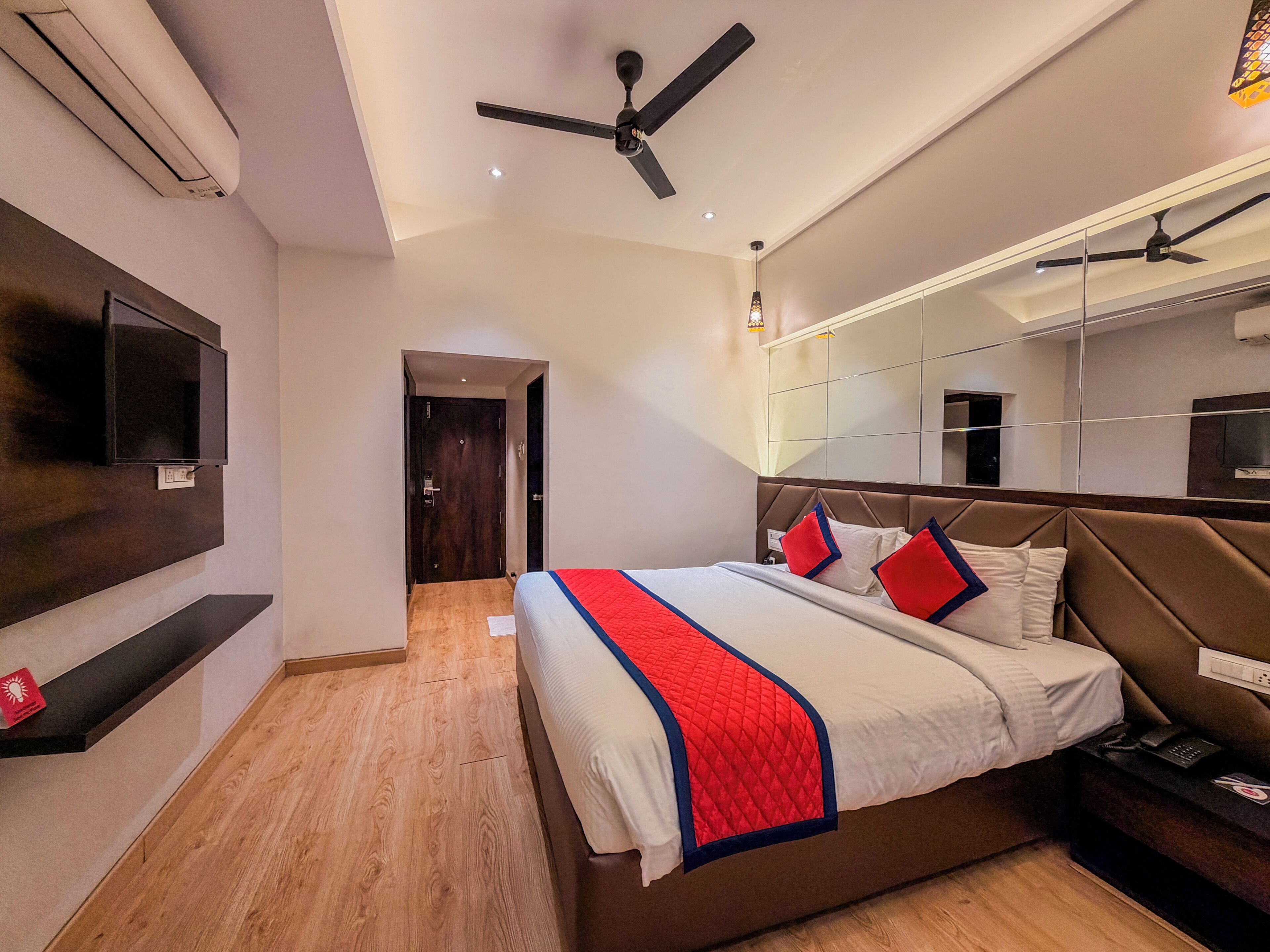 A modern hotel room with a bed, a TV, a ceiling fan, and a mirror.