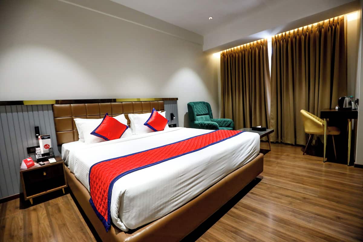 A hotel room with a large bed, a desk, a chair, and a nightstand.