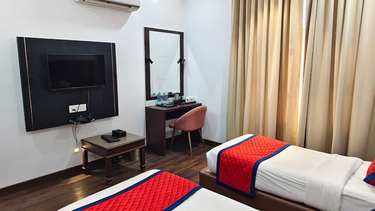 A hotel room with a TV, desk, chair, two beds, and a mirror.