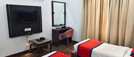 A hotel room with a TV, desk, chair, two beds, and a mirror.