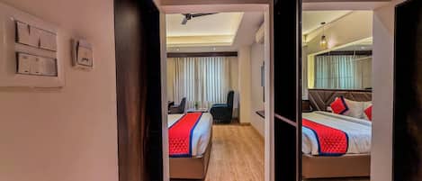 A hotel room with a mirrored closet, a bed with a red and blue quilt, a desk, and a chair.