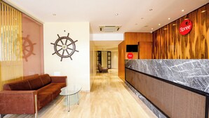 A hotel reception area with a wooden reception desk, a leather sofa, and a ship's wheel decoration on the wall. - Spree Manor Hotel (Chhatrapati Sambhajinagar)