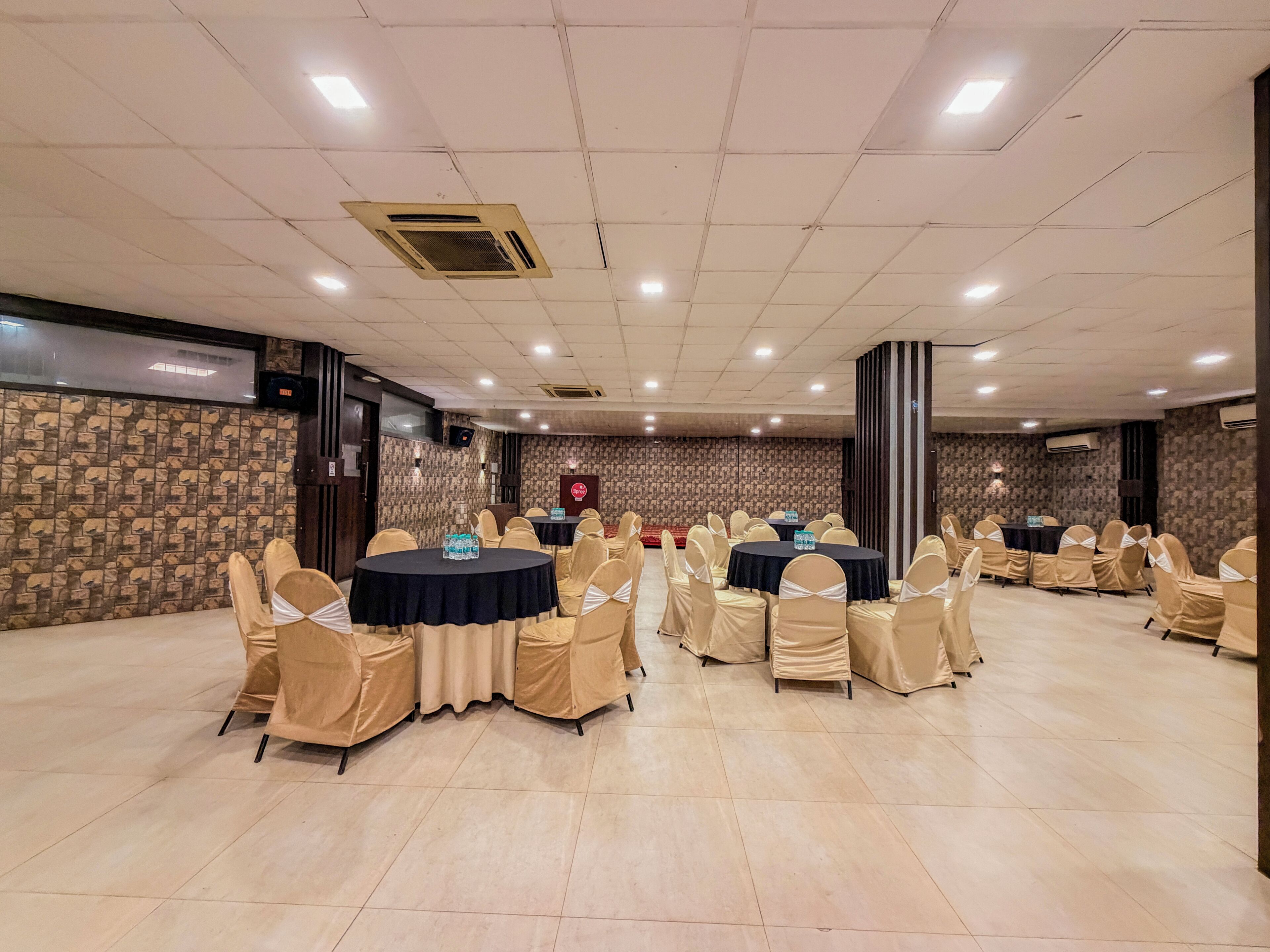 A conference room with multiple round tables, beige chairs, and a patterned wall.