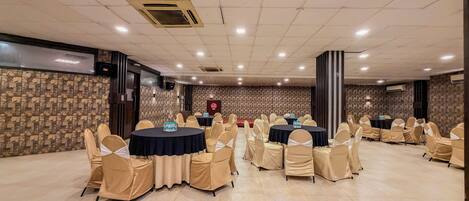 A conference room with multiple round tables, beige chairs, and a patterned wall.
