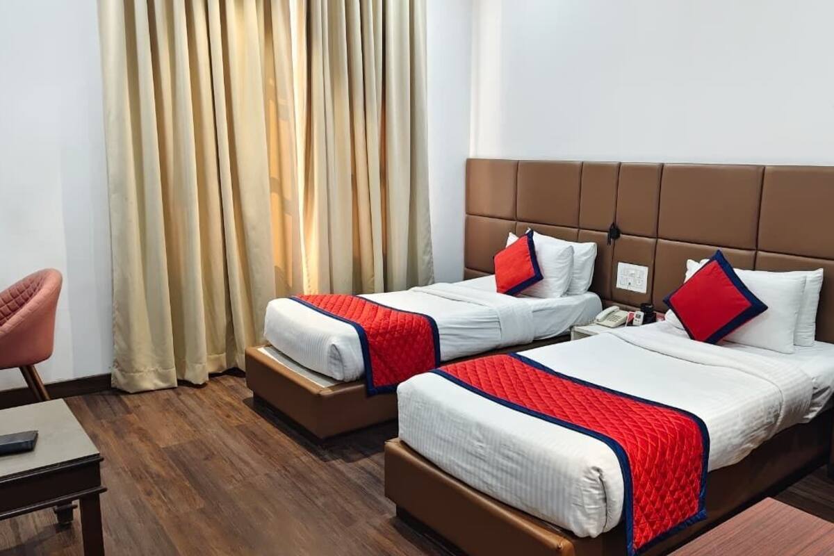 A hotel room with two beds, a desk, a chair, and a window with curtains.