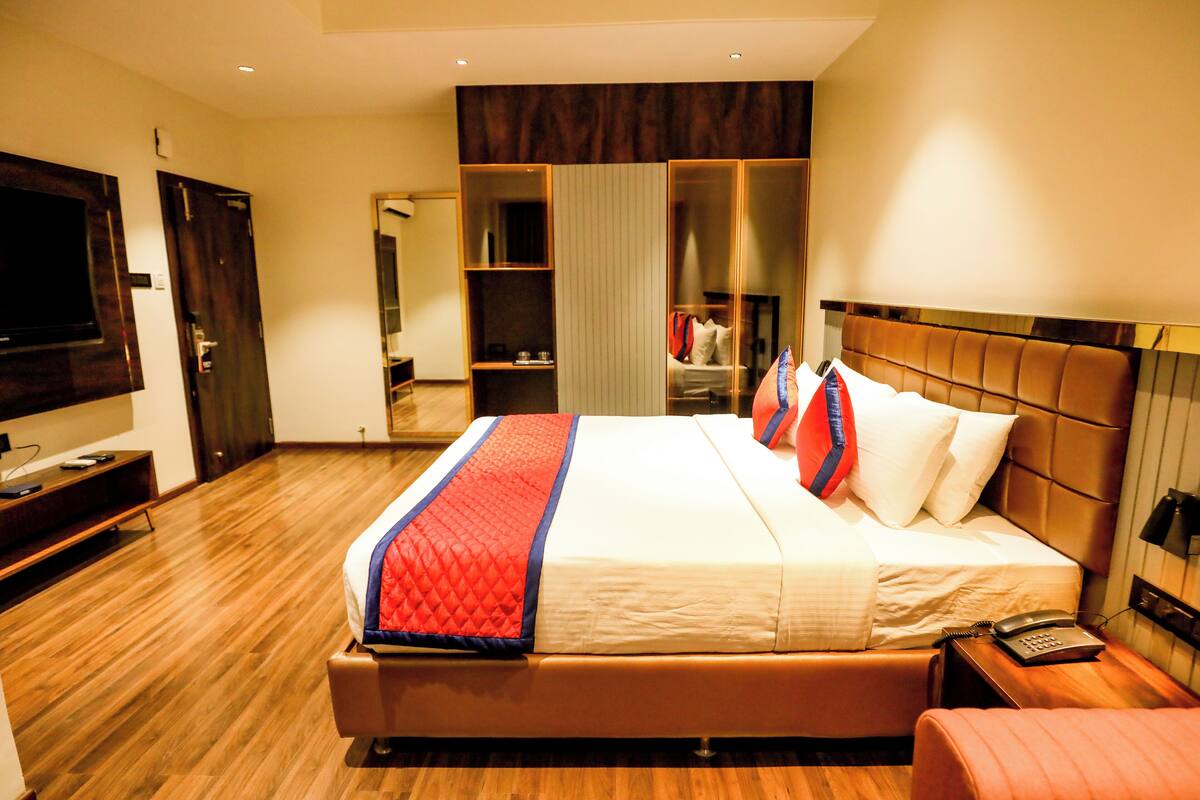 A hotel room with a large bed, a bedside table with a phone, a TV on the left, and a wardrobe with a mirror.