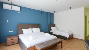 Une chambre d’hôtel avec deux lits, un banc, un plancher en bois et un mur d’accent bleu.