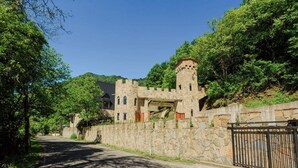 Une structure ressemblant à un château, avec un mur de pierre, une porte et une route menant à l’entrée.