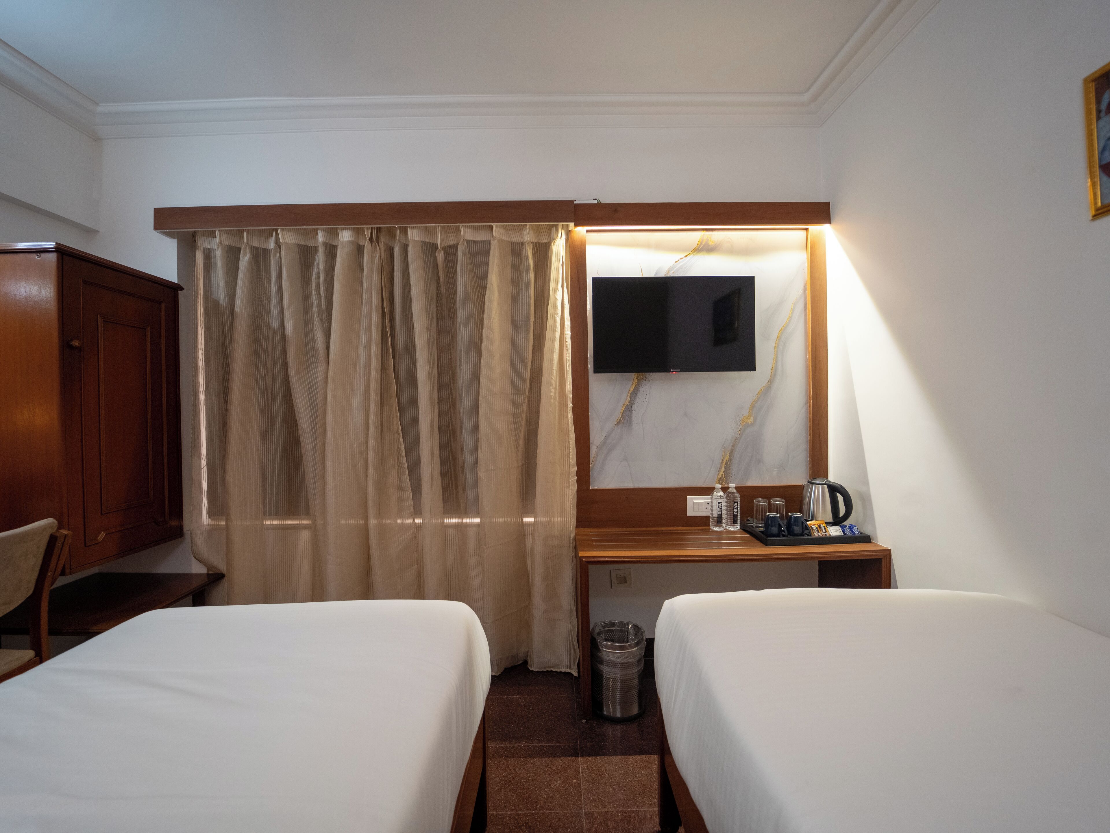 Habitación de hotel con dos camas, un escritorio con cafetera, televisor y cortina.