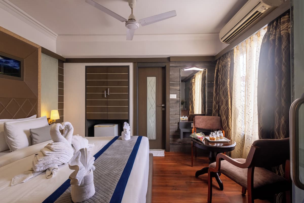 A hotel room with a bed, a chair, a small table with a tray of food, and a ceiling fan.