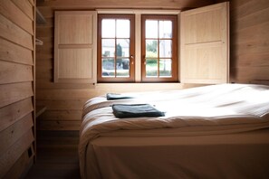 A wooden room with a bed, a window with wooden shutters, and a view of the outside. - Cozy Cabins in Vencimont (Vencimont)
