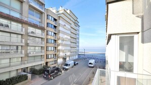 Ein mehrstöckiges Wohngebäude mit Balkonen, einer Straße davor und Blick aufs Meer.