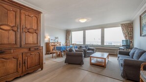 Amplia sala de estar con un gran aparador de madera, una zona de comedor con mesa azul a cuadros y vistas al mar a través de amplias ventanas.