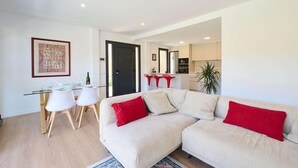 A modern living room with a beige sofa, a glass dining table, and a red accent pillow. - Villa in Lloret de Mar with Private Pool (Vidreres)