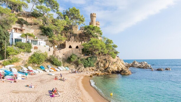 A beach with a castle on a cliff, boats on the shore, and clear blue water. - Villa in Lloret de Mar with Private Pool (Vidreres)