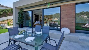An outdoor dining area with a glass table and chairs, a potted plant, and a view of the surrounding landscape. - Villa in Lloret de Mar with Private Pool (Vidreres)
