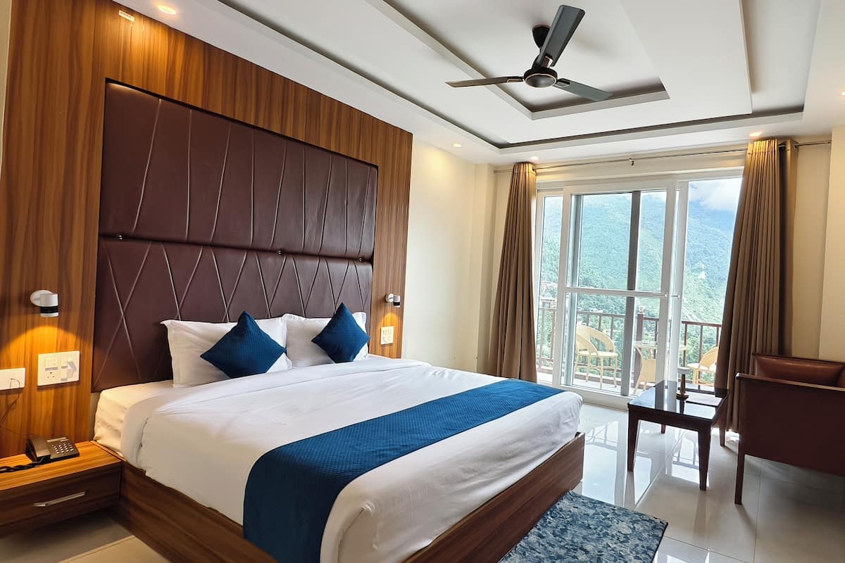 A hotel room with a large bed, a desk, a chair, a ceiling fan, and a view of the mountains.