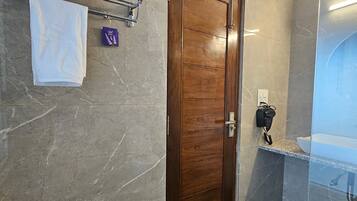 A modern bathroom with a wooden door, marble walls, a glass shower enclosure, and a towel rack with folded towels.