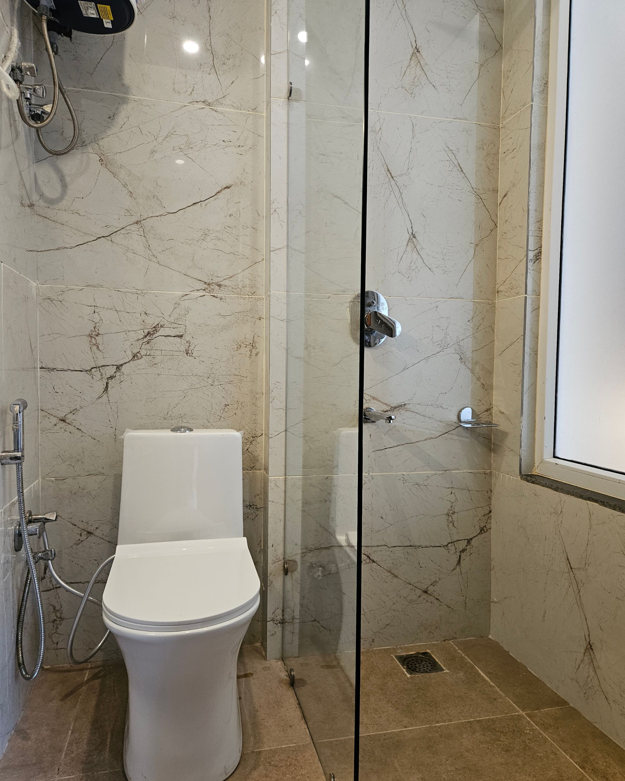 A bathroom with a toilet, a shower with a glass door, and a marble-tiled wall.