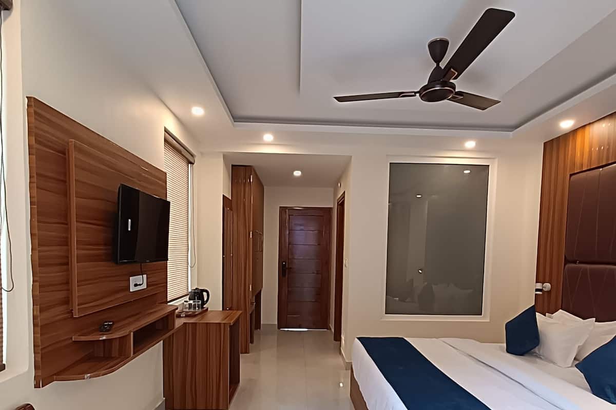 A hotel room with a bed, a TV mounted on the wall, a desk, a chair, and a ceiling fan.