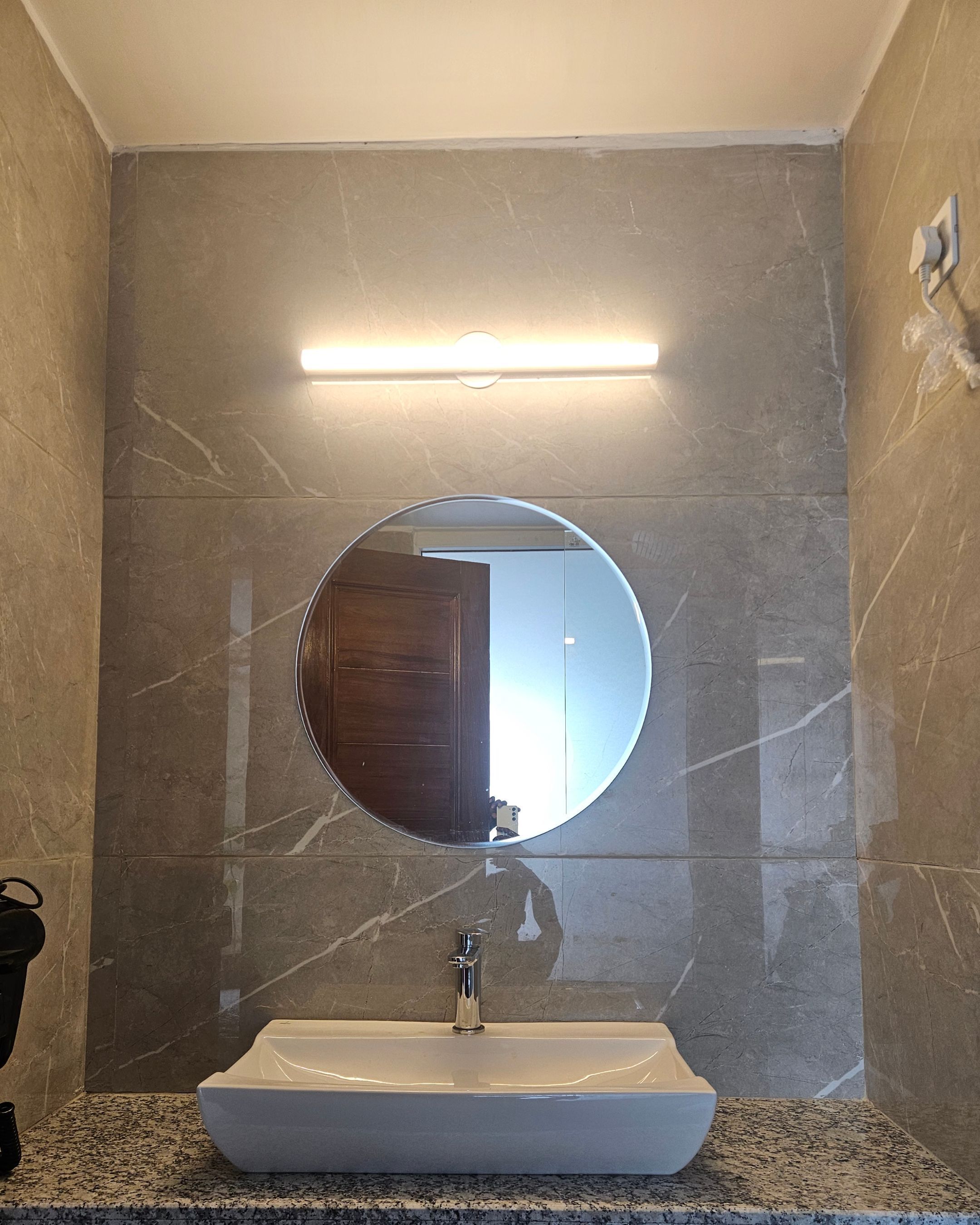 Een badkamer met een ronde spiegel, een witte wastafel en een wandlamp.
