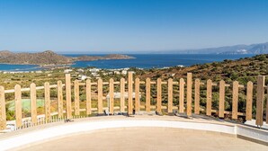 Une terrasse avec vue sur la mer et les collines, une clôture en bois et une zone dallée.
