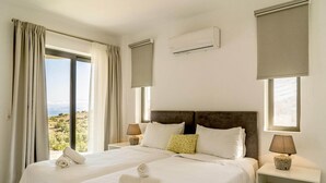 Une chambre d’hôtel avec deux lits, une grande fenêtre avec des rideaux, un appareil de climatisation et une table de chevet avec une lampe.