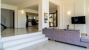 Un salon moderne avec un grand canapé gris, un téléviseur à écran plat fixé au mur et un escalier menant à un autre espace.