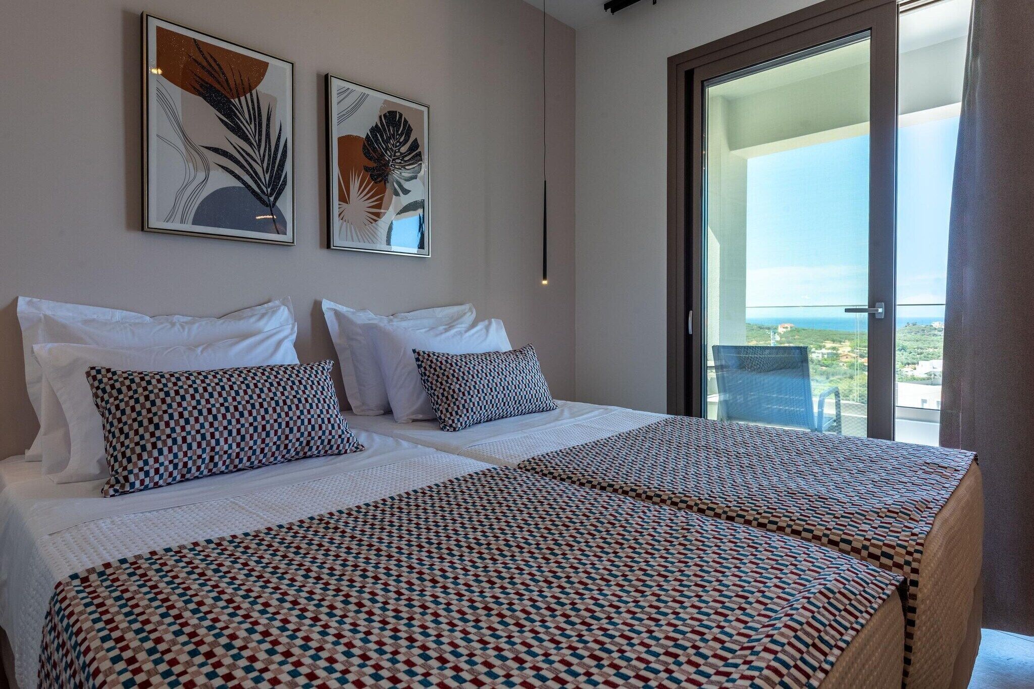 Habitación de hotel con dos camas, un balcón con vistas y dos cuadros enmarcados en la pared.
