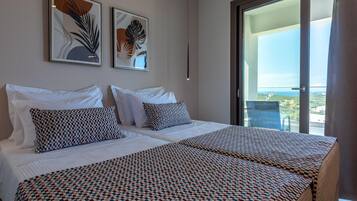 Habitación de hotel con dos camas, un balcón con vistas y dos cuadros enmarcados en la pared.