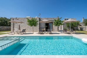 A swimming pool with lounge chairs and umbrellas, surrounded by stone walls and trees. - Villa in Koxare with Private Pool & Garden (Rethymno)