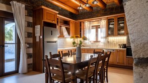 A kitchen with wooden cabinets, a stainless steel refrigerator, and a dining table with chairs. - Charming Family Villa with Pool in Koxare (Rethymno)