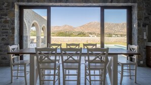 A dining area with a stone wall and large windows overlooking a mountainous landscape. - Charming Family Villa with Pool in Koxare (Rethymno)