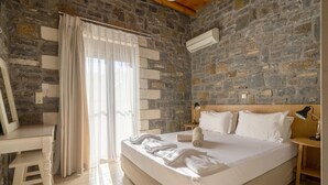 A bedroom with a stone wall, a bed with white linens, a desk, and a chair. - Charming Family Villa with Pool in Koxare (Rethymno)