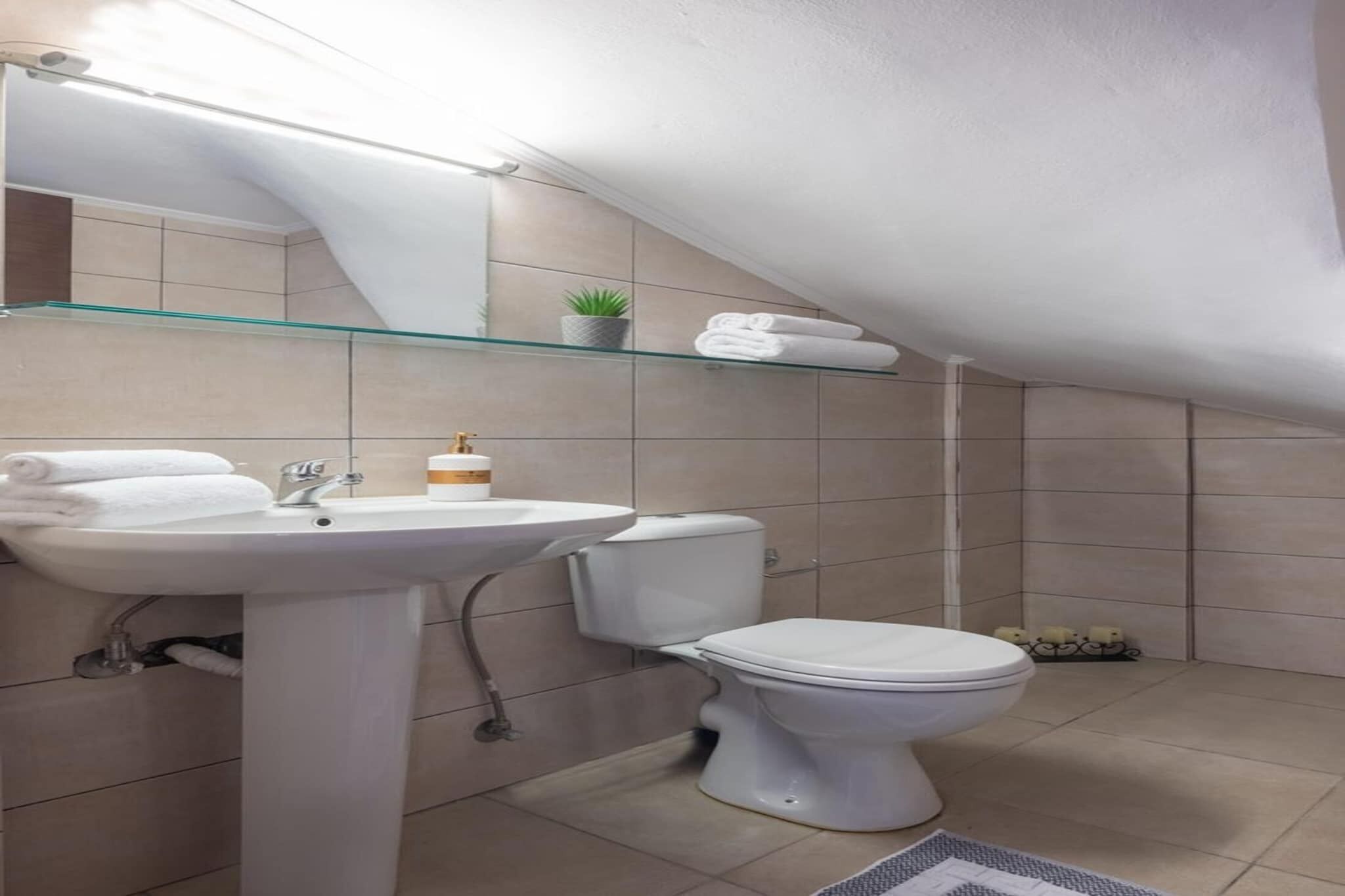 A modern bathroom with a white sink, toilet, and glass shelf above the toilet.