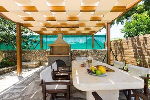 Um pátio externo com parede de pedra, pérgola de madeira e forno de tijolos.