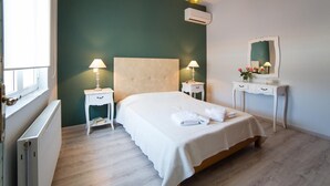 A bedroom with a bed, bedside tables, a dresser, a mirror, and an air conditioning unit.