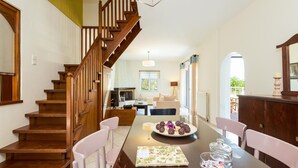 A spacious dining area with a wooden staircase, a dining table set with a plate of cookies, and a view into the living room.