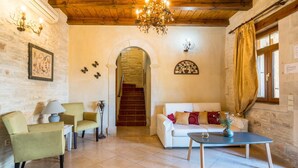 A cozy living room with a white sofa, yellow armchairs, a coffee table, and a chandelier. A staircase leads to an upper level. - Villa in Rethymno with countryside view (Rethymno)