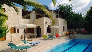 A poolside area with lounge chairs and umbrellas, a stone building with arched doorways, and a clear blue pool. - Villa in Rethymno with countryside view (Rethymno)