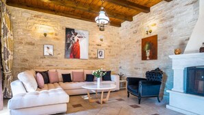 A cozy living room with a stone wall, a white sofa, a round coffee table, and a fireplace. - Villa in Rethymno with countryside view (Rethymno)
