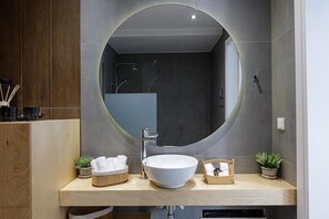 Un baño moderno con un espejo redondo, un lavabo blanco y un mueble de tocador de madera.