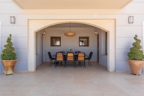 An outdoor dining area with a table and chairs, an arched entrance, and potted plants.