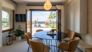 Un espace repas moderne avec une table ronde et des chaises, un luminaire suspendu et une vue sur une piscine et des palmiers.