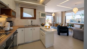 Une cuisine moderne dotée d’un îlot central, d’un coin repas avec une table et des chaises, et d’une grande fenêtre offrant une vue sur l’extérieur.
