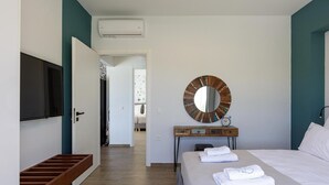 A hotel room with a bed, a round mirror, a bedside table with a clock, and a TV mounted on the wall.