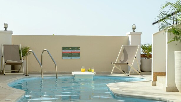 A swimming pool with two metal ladders, two lounge chairs, and a small table with a bottle and glass. - Villa in Rethymno with Pool & Jacuzzi (Rethymno)