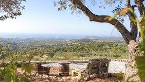 A rustic outdoor seating area with wooden furniture and barrels, overlooking a scenic landscape with hills and a distant view of the sea. - Villa in Rethymno with Pool & Jacuzzi (Rethymno)
