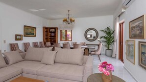 A living room with a beige sofa, a dining table with chairs, a chandelier, and a potted plant. - Villa in Rethymno with Pool & Jacuzzi (Rethymno)