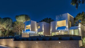 A modern two-story house with a flat roof, large windows, and a well-lit exterior.